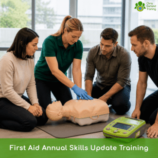 A first aid training session showing four adults gathered around a CPR mannequin torso on a gray floor mat. A woman in a green polo shirt and blue medical gloves is demonstrating proper hand placement on the mannequin's chest while another woman and two men watch intently. An AED training unit sits on the floor in the foreground. A logo for "Garland Training" is in the top right, and a bright green banner at the bottom reads "First Aid Annual Skills Update Training."