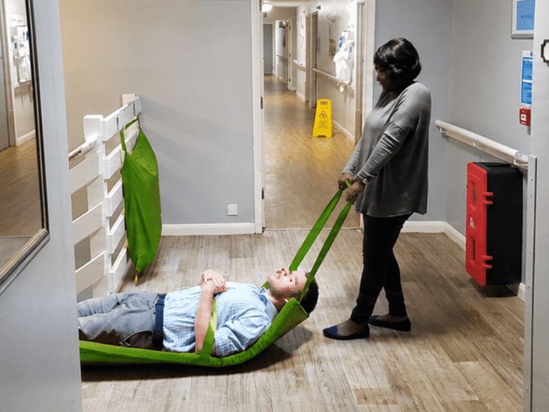 Trainee practicing handling procedures with a red evacuation sledge in a care home corridor during a regulated training course in Knutsford.